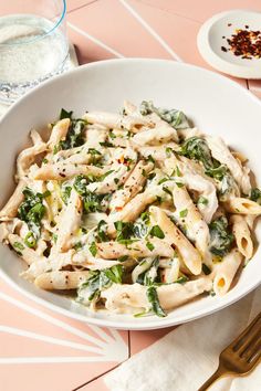 a white bowl filled with pasta and spinach on top of a pink table cloth