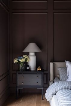 a bedroom with a bed, nightstand and lamp on the side table in front of it