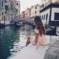 a woman sitting on the edge of a bridge looking out over a canal in venice