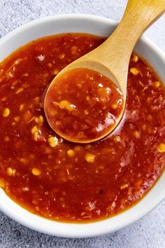 a wooden spoon in a white bowl filled with chili sauce