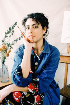 a woman sitting on a chair with a pencil in her hand and looking at the camera