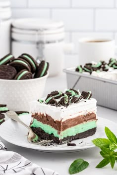 a piece of cake on a plate with oreo cookies and mint leaves in the background