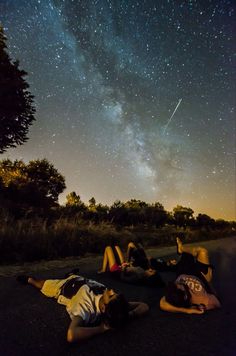 three people are laying on the ground watching the stars