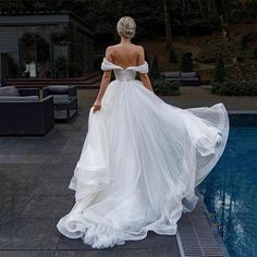 a woman in a white dress is standing near a pool with her back to the camera