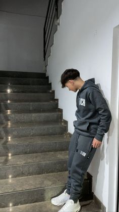 a young man leaning against the wall in front of some stairs with his head down