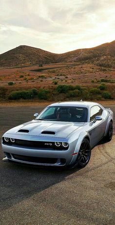 a silver sports car parked in the middle of an empty parking lot with mountains in the background