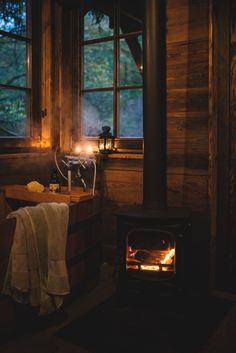 a wood burning stove inside of a wooden cabin next to a bath tub and window