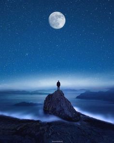 a man standing on top of a mountain under a full moon filled sky with stars