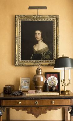 a painting hangs on the wall above a table with an antique lamp and other items