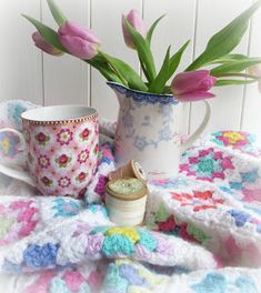 pink tulips in a crocheted vase on a table next to a coffee cup