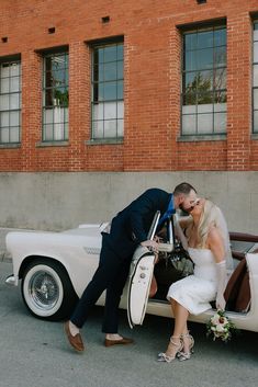 a bride and groom kissing in front of an old fashioned car with the door open