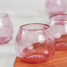 three pink glass vases sitting on top of a wooden table next to each other