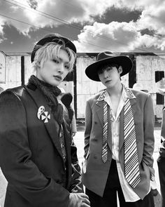 two young men standing next to each other in front of a building and cloudy sky