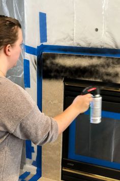 a woman is painting the wall in front of an oven with blue tape on it