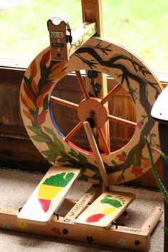 a wooden spinning wheel sitting on top of a floor next to a window sill