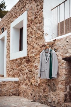 a suit and tie hanging on a stone wall next to a window with shutters