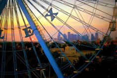 a ferris wheel with the city skyline in the background at sunset or sunrise, as seen from an amusement park