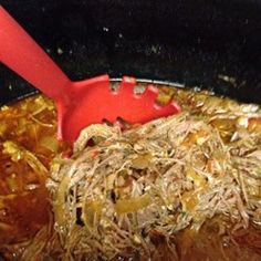 a red spatula in a pot filled with shredded noodles and meats on the stove