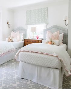 two twin beds in a bedroom with white walls and pink pillows on the headboards