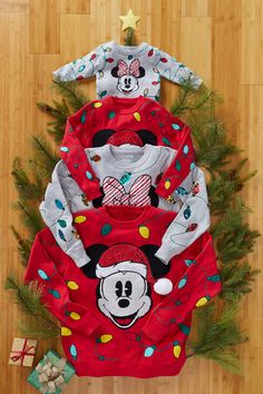 three children's mickey mouse pajamas on top of a wooden floor next to christmas decorations