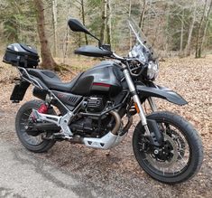 the motorcycle is parked on the side of the road near some trees and fallen leaves