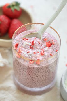 there is a bowl of strawberries and a glass of milk with a spoon in it