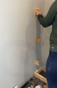 a woman standing in front of a wall with some wood pieces on the floor next to it