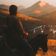 a man riding on the back of a black horse next to a lush green hillside