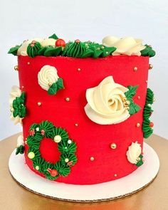 a red and white christmas cake with holly wreaths on the top is sitting on a table