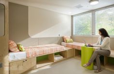 a woman sitting on a bench in a room with two beds and a desk next to it