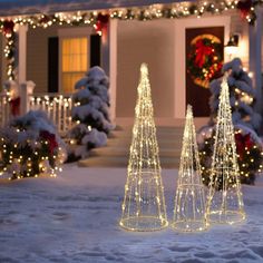 three lighted christmas trees in front of a house