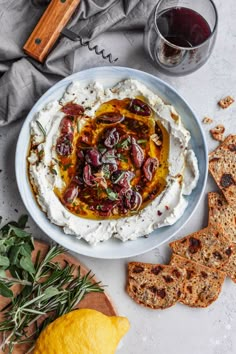 a bowl of mashed potatoes with olives and herbs on the side next to crackers