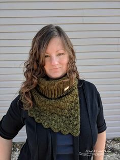 a woman standing in front of a white building wearing a green cowl neck scarf