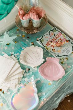 the table is decorated with seashells and confetti for a mermaid themed birthday party