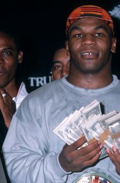 a man is holding stacks of money in his hands and looking at the camera while others look on