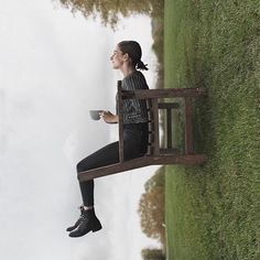 a woman sitting on a bench holding a coffee cup and looking up at the sky