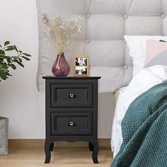 a bedroom with a white headboard and black night stand next to a plant in a vase