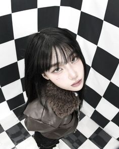 a woman with black hair and bangs standing in front of a checkerboard wall