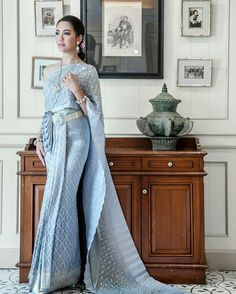 a woman standing in front of a dresser wearing a blue dress with silver lace on it