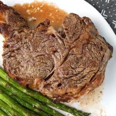 a piece of steak and asparagus on a white plate with brown gravy