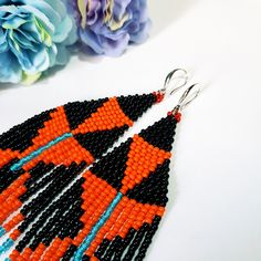 an orange and black beaded earrings on a white table next to some blue flowers