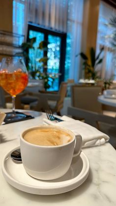 a cup of coffee sitting on top of a white plate next to a glass of wine