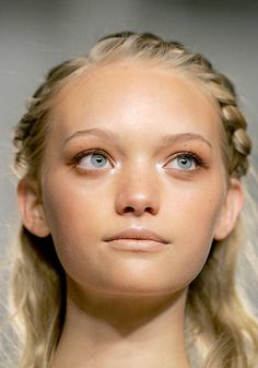 a woman with blonde hair and blue eyes looks at the camera while wearing braids