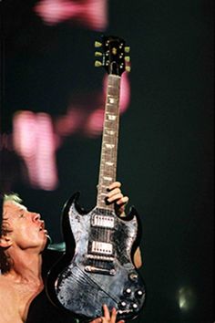 a shirtless man holding an electric guitar in his right hand and looking up at the sky