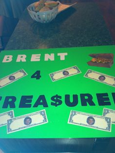 a green sign that says brent 4 treasures with dollar bills on it and a bowl of chips in the background