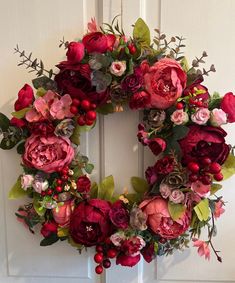 a wreath with red flowers and greenery hangs on a door handle in front of a white door