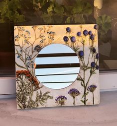 a mirror with flowers painted on it sitting in front of a window sill next to a potted plant