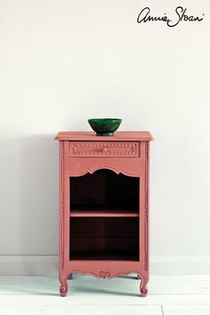 a small pink cabinet with a green bowl on it's top and bottom shelf