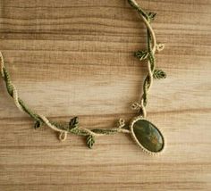 a necklace with green beads and leaves is on a wooden surface in front of a wall