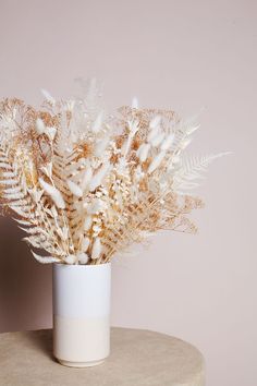 a vase filled with white flowers on top of a table next to a pink wall